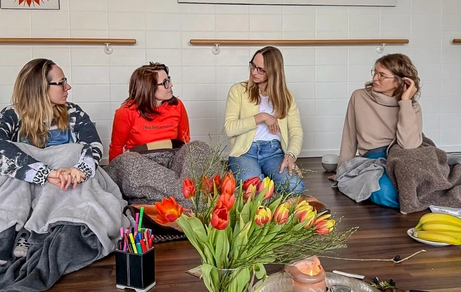 Gruppe im Sitzkreis auf dem Boden im Herzstudio Neufarn, mit Decken und Blumen